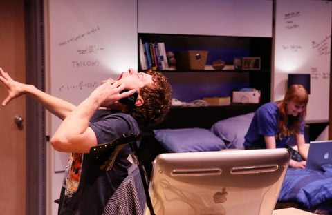 Matt Holzfeind flings an arm back at his desk while Rae Gray sits on the bed